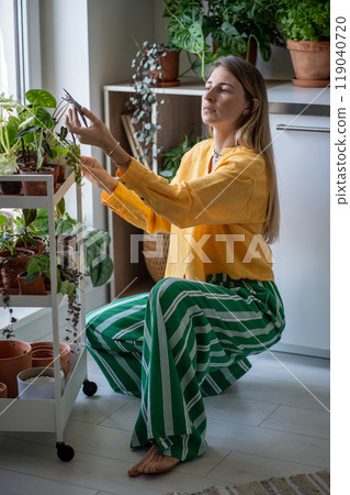 Mindful florist examines home greenhouse, carefully checking condition each leaf loved houseplants. Mindful florist examines home greenhouse, carefully checking condition each leaf loved houseplants. 119040720