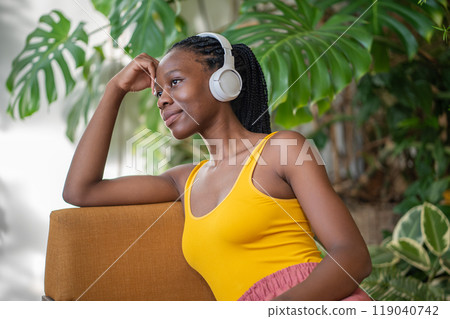 Dreaming calm smiling black woman in headphones listening to relaxed music in urban jungle interior. Dreaming calm smiling black woman in headphones listening to relaxed music in urban jungle interior. 119040742
