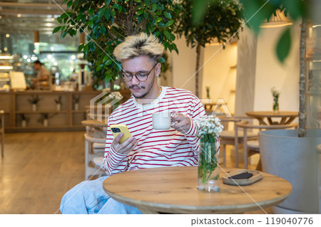Thoughtful dreamy freelancer man drinking coffee at cafe table, using mobile phone. Coffee break. Thoughtful dreamy freelancer man drinking coffee at cafe table, using mobile phone. Coffee break. 119040776