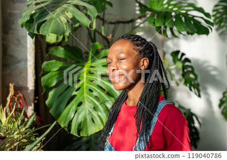 Pleased African American young woman stands by window, basking in sunlight with smile face feel joy. 119040786