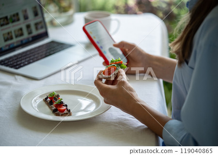 Hand holding bread cracker topped with cream cheese, tomatoes, fresh herbs take breakfast with phone Hand holding bread cracker topped with cream cheese, tomatoes, fresh herbs take breakfast with phone 119040865