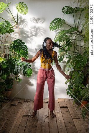 Positive black girl dancing barefoot on wooden floor in headphones listening to music enjoy moment. 119040878