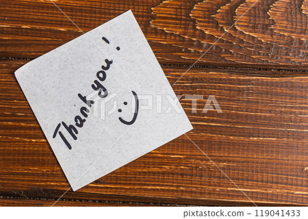 A thank you note is written on a piece of paper and placed on a wooden surface. 119041433