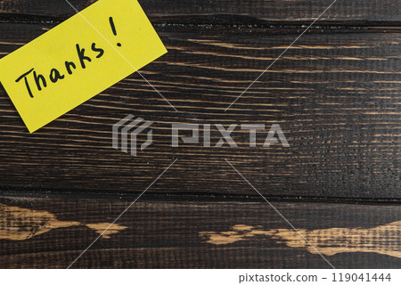 A small note with the word thank you on a brown wooden table background A small note with the word thank you on a brown wooden table background 119041444