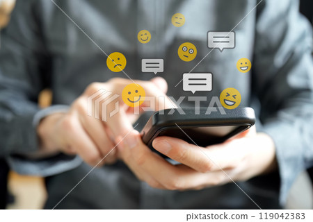 Emojis with various facial expressions, such as smiling faces, and speech bubbles for messages are floating above the smartphone. 119042383