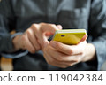 A person tapping a yellow smartphone with their index finger 119042384