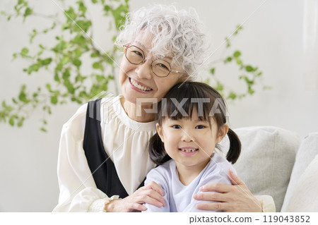 Grandmother snuggling with her grandson in the living room, looking at the camera 119043852