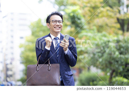 商務中年男子一邊看智慧型手機一邊握拳 商務中年男子一邊看智慧型手機一邊握拳 119044653