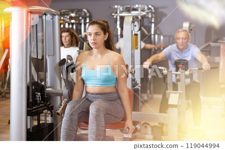 Portrait of young woman during workout with power exercise machine in gym 119044994