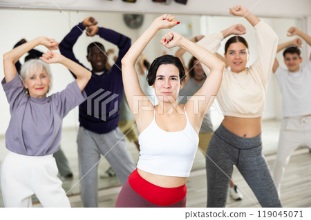 Happy young woman practising modern dance moves with other people in dance studio Happy young woman practising modern dance moves with other people in dance studio 119045071