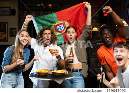 Excited diverse football supporters with flag of Portugal with pint of beer and chips in the pub Excited diverse football supporters with flag of Portugal with pint of beer and chips in the pub 119045092