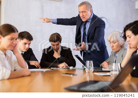 Outraged old manager getting mad at young adult mature office workers sitting with reports and laptops at table in meeting room 119045241