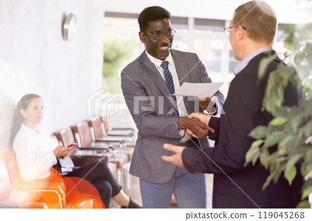 Middle-aged man handshaking with other person in waiting room Middle-aged man handshaking with other person in waiting room 119045268