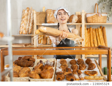 Young woman seller took fresh bagguetes of white flour out of window in bakery 119045324