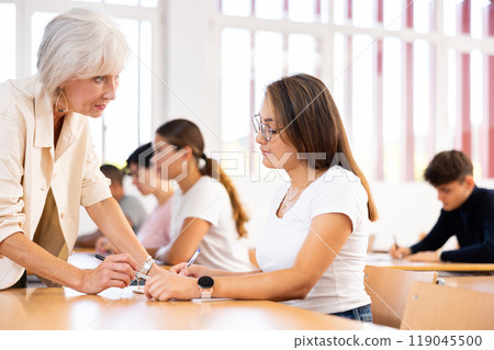 Senior woman teacher helping student with task solution 119045500