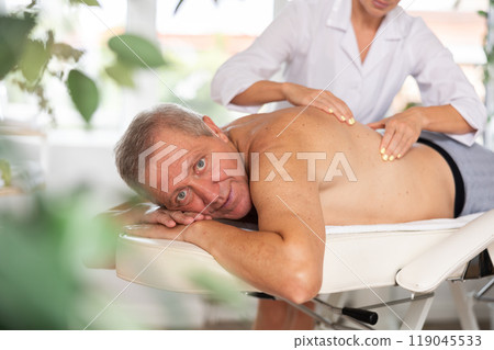 Relaxed old man having back massage therapy conducted by skilled masseuse Relaxed old man having back massage therapy conducted by skilled masseuse 119045533