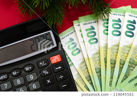 Calculator, 100 euro banknotes and the inscription 2025 new year with spruce branches on a red background, economic crisis, tax time 119045581