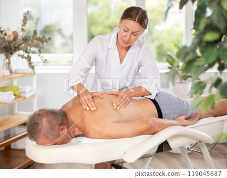masseuse giving massage to male patient masseuse giving massage to male patient 119045687