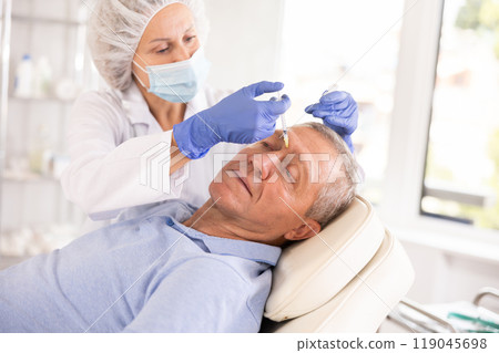 Doctor performs procedure of injectable correction of wrinkles in nasal bridge area for man 119045698