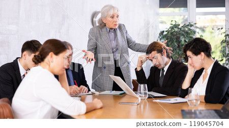 Irritated elderly female boss reprimanding subordinates in office Irritated elderly female boss reprimanding subordinates in office 119045704