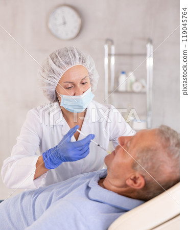 Concentrated female cosmetologist performing face contouring injections to elderly man 119045764