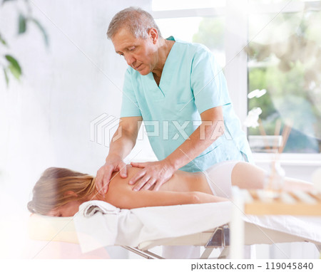 Skilled old masseur conducting back massage for woman client 119045840