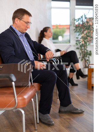 Middle-aged male visitor sitting on the bench in waiting room of clinic Middle-aged male visitor sitting on the bench in waiting room of clinic 119045850