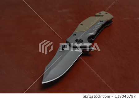 An unfolded tactical military knife with a sharp blade. Tool against the natural leather. An unfolded tactical military knife with a sharp blade. Tool against the natural leather. 119046797
