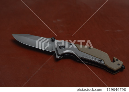 An unfolded tactical military knife with a sharp blade. Tool against the natural leather. An unfolded tactical military knife with a sharp blade. Tool against the natural leather. 119046798
