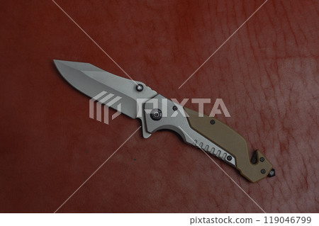 An unfolded tactical military knife with a sharp blade. Tool against the natural leather. An unfolded tactical military knife with a sharp blade. Tool against the natural leather. 119046799