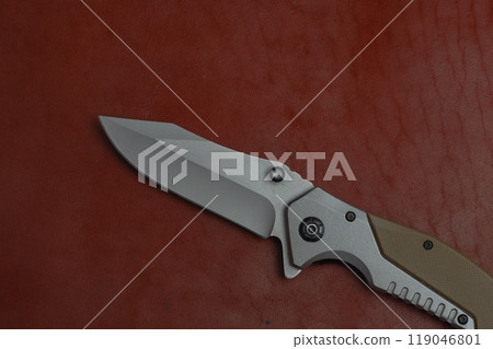 An unfolded tactical military knife with a sharp blade. Tool against the natural leather. An unfolded tactical military knife with a sharp blade. Tool against the natural leather. 119046801