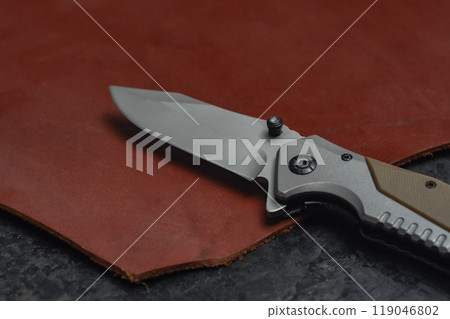 An unfolded tactical military knife with a sharp blade. Tool against the natural leather. 119046802