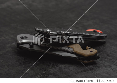 Two folded tactical military knives on a dark concrete background. 119046808