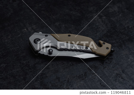 Closed tactical military knife with sharp blade. Tool on dark concrete background. Closed tactical military knife with sharp blade. Tool on dark concrete background. 119046811
