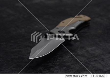 An unfolded tactical military knife with a sharp blade. Tool on dark concrete background. 119046812