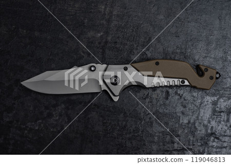An unfolded tactical military knife with a sharp blade. Tool on dark concrete background. An unfolded tactical military knife with a sharp blade. Tool on dark concrete background. 119046813