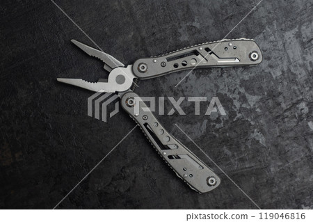 Tactical outdoor multi-tool with pliers, blade, screwdriver and other tools on a dark concrete background. Universal multitool for tourism and repair. Tactical outdoor multi-tool with pliers, blade, screwdriver and other tools on a dark concrete background. Universal multitool for tourism and repair. 119046816
