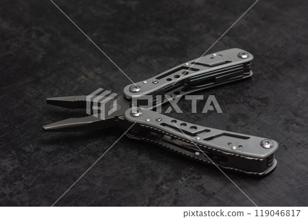 Tactical outdoor multi-tool with pliers, blade, screwdriver and other tools on a dark concrete background. Universal multitool for tourism and repair. 119046817
