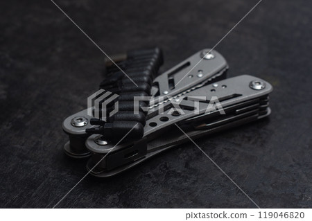 Tactical outdoor multi-tool with pliers, blade, screwdriver and other tools on a dark concrete background. Universal multitool for tourism and repair. 119046820