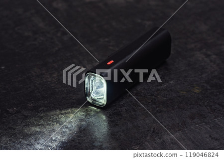Small black bicycle light with a beam of light, rests on a dark table. Small black bicycle light with a beam of light, rests on a dark table. 119046824