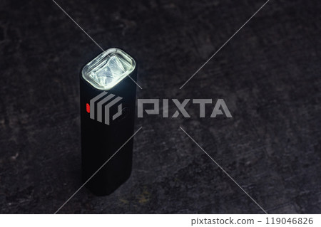 Small black bicycle light with a beam of light, rests on a dark table. Small black bicycle light with a beam of light, rests on a dark table. 119046826