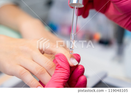 Manicurist applying an oil for cuticulas removing from the nail during manicure session Manicurist applying an oil for cuticulas removing from the nail during manicure session 119048105