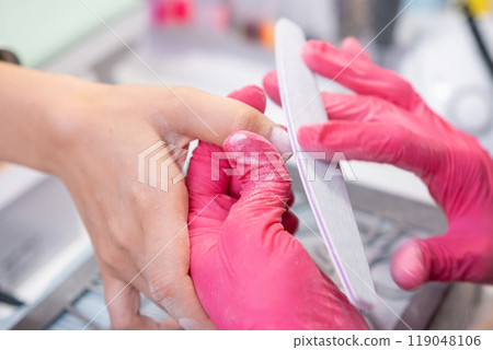 Nail master in pink gloves polishes the clients nails with a nail file Nail master in pink gloves polishes the clients nails with a nail file 119048106