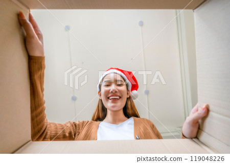 Low angle view of surprised young Asian woman wearing Christmas hat and unpacking Low angle view of surprised young Asian woman wearing Christmas hat and unpacking 119048226