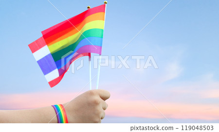 Cut out of hand holding both the LGBT flag and Thailand flag, set against blue sky background with clipping paths. The symbolizing unity, diversity, and inclusion. 119048503