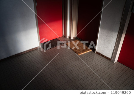 A serene hallway with red doors, featuring doormats on tiled floors softly illuminated by natural light, creating a warm and welcoming ambience. A serene hallway with red doors, featuring doormats on tiled floors softly illuminated by natural light, creating a warm and welcoming ambience. 119049260