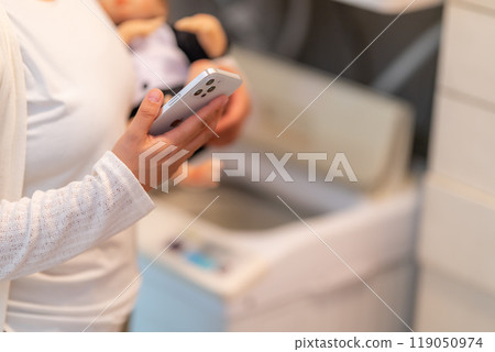 A housewife who doesn't let go of her smartphone while doing housework A housewife who doesn't let go of her smartphone while doing housework 119050974