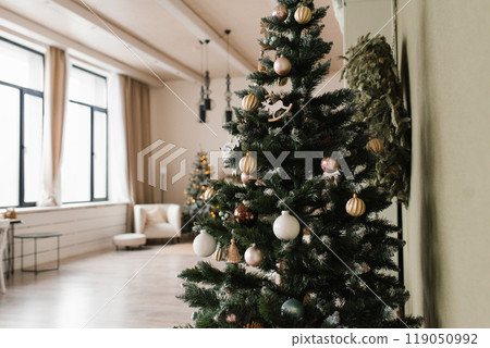 Large Christmas tree with many ornaments sits in a room with a window Large Christmas tree with many ornaments sits in a room with a window 119050992