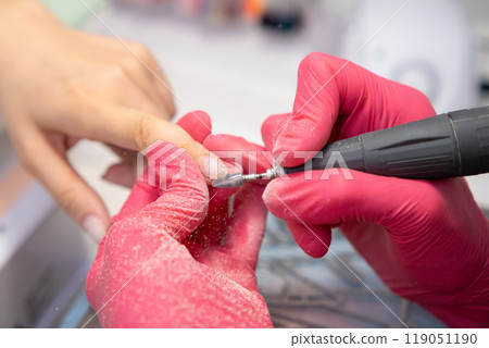 Skilled technician using a nail drill machine for manicure on client in a salon. Skilled technician using a nail drill machine for manicure on client in a salon. 119051190