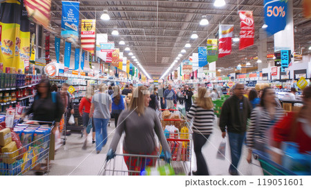 Blurred motion of people in supermarket. Wide-angle shot of a busy store with colorful sale banners hanging from the ceiling. Shopping carts filled with products are in the foreground. 119051601